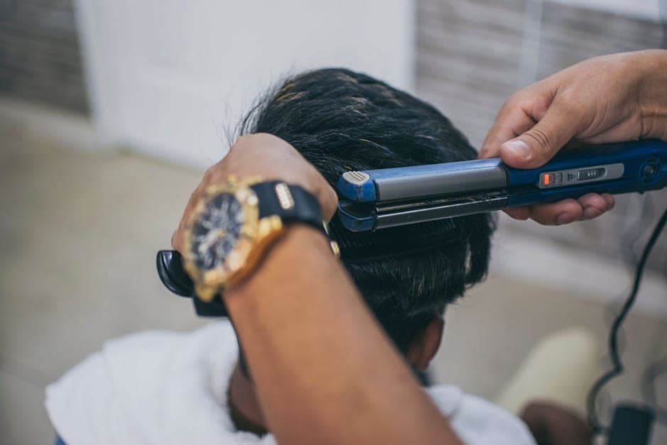 A heated straightening iron being drawn through hair in a barbershop
