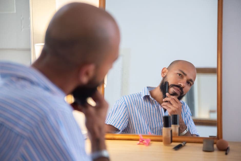 A man grooming his beard in front of a mirror