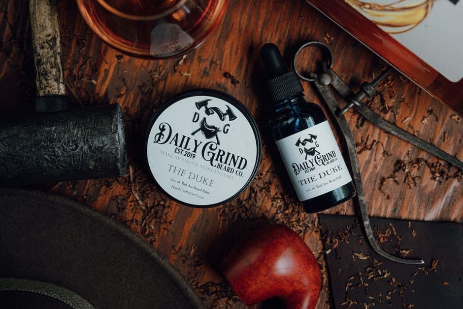 A tin of beard balm and a bottle of beard oil on a wooden surface