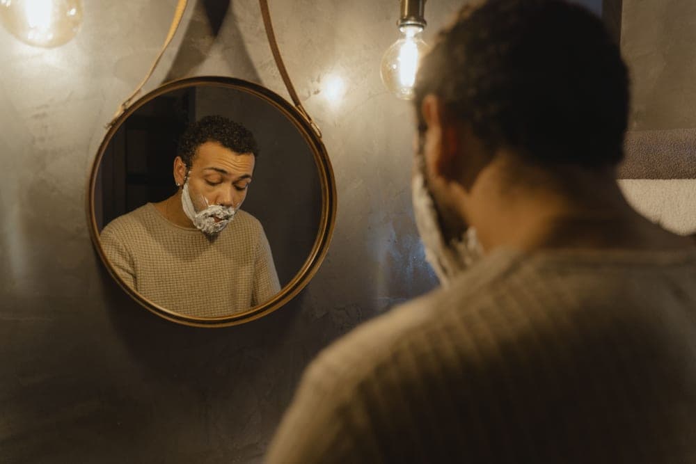 A man trimming his beard in front of a bathroom mirror