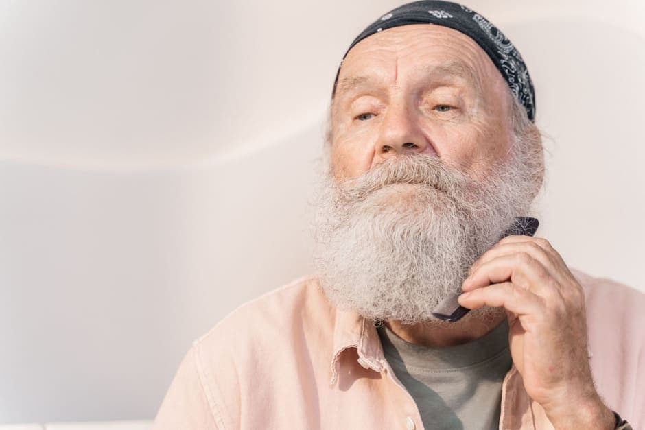 A man with a full gray beard combing it through with his hand
