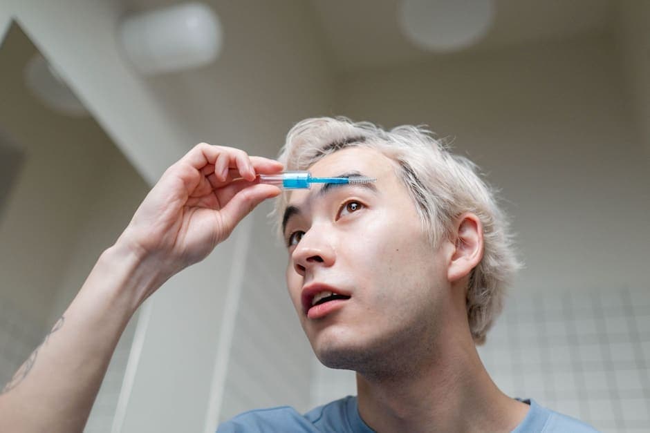 A man grooming his eyebrow in front of a bathroom mirror