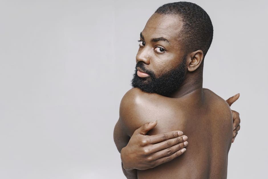 A shirtless man with a trimmed beard against a plain background