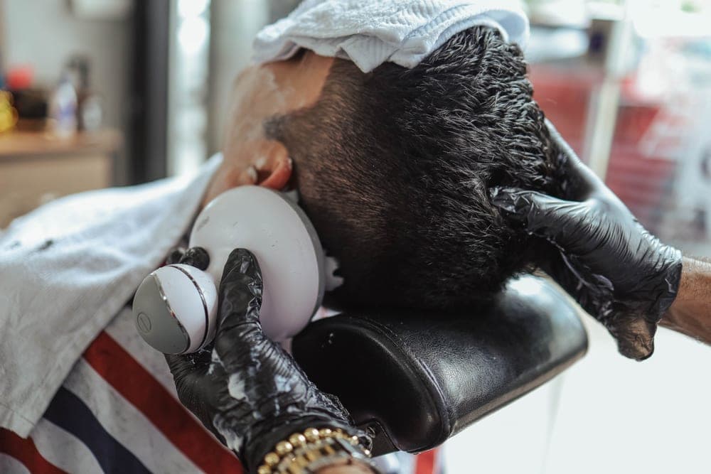 An electric shaver head disassembled beside a cleaning brush