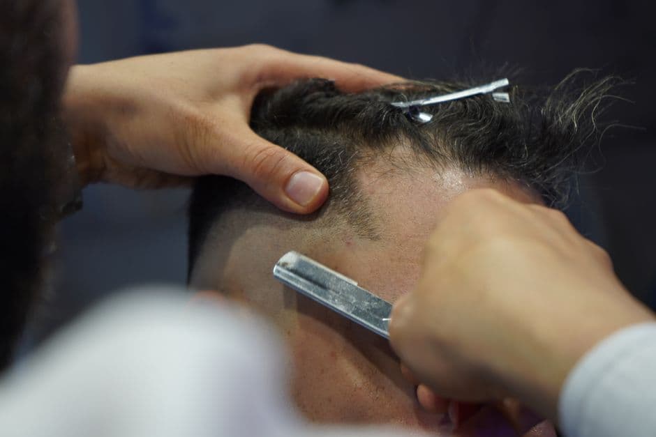 A barber shaving a client's head with a blade