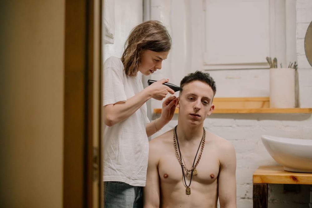 A man cutting his own hair with clippers in front of a mirror
