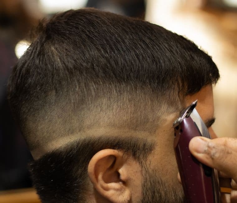 A barber using clippers to finish a fade haircut
