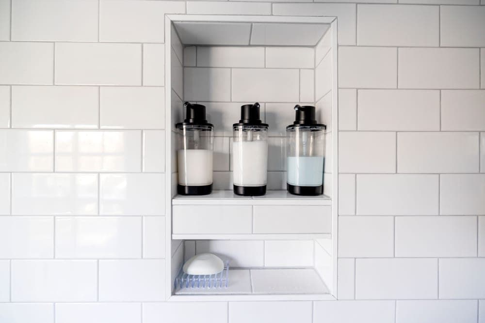 A shampoo bottle on a tiled shower shelf