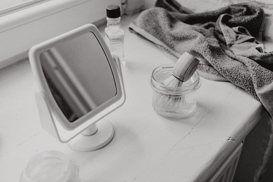 A shaving brush and mirror on a minimalist bathroom counter, in black and white