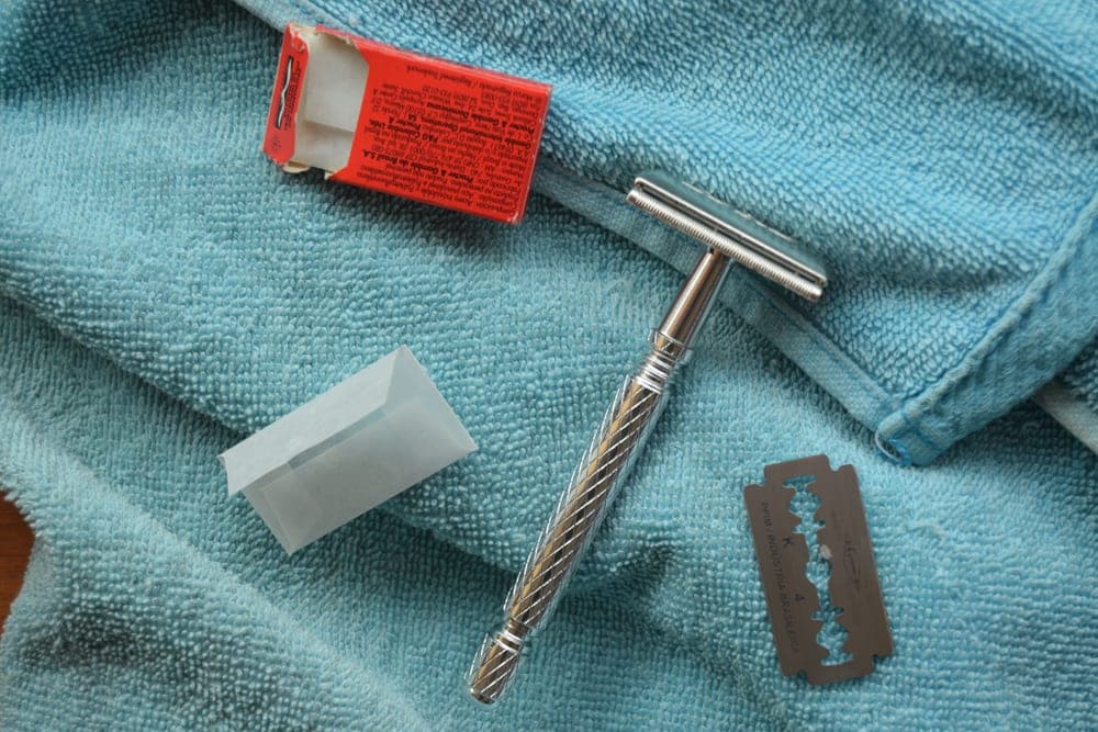A disassembled safety razor beside a towel