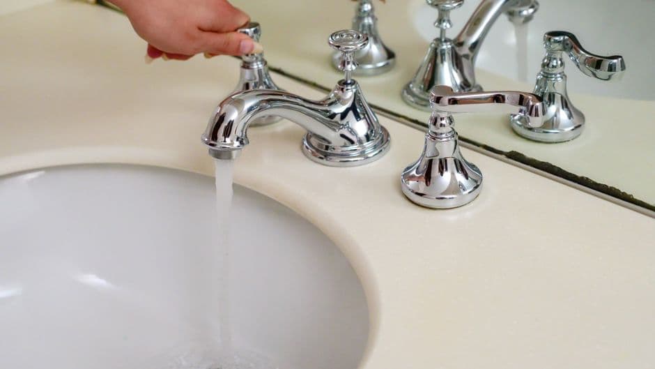 A hand running a chrome bathroom faucet