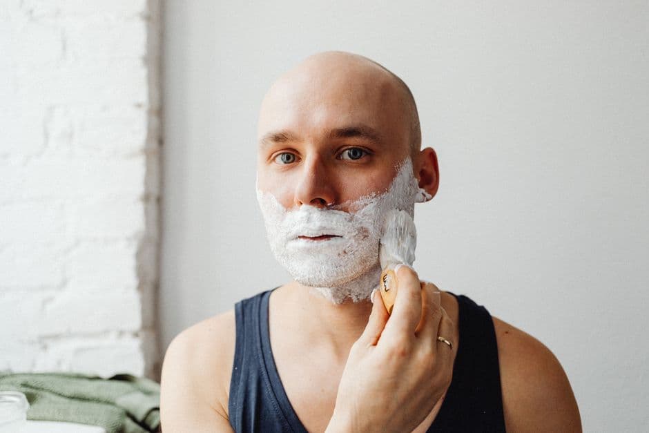A man shaving his head at a bathroom mirror