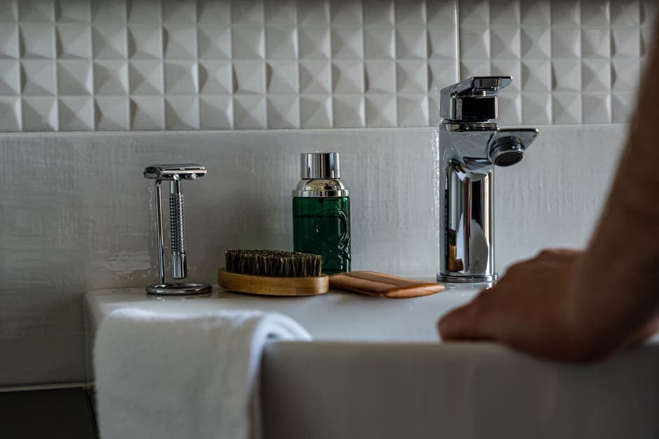 A safety razor, brush and aftershave beside a bathroom sink with a folded towel