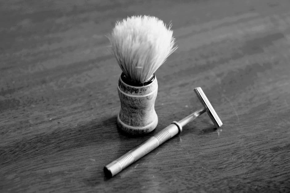 A classic shaving brush and razor on a wooden table, in black and white