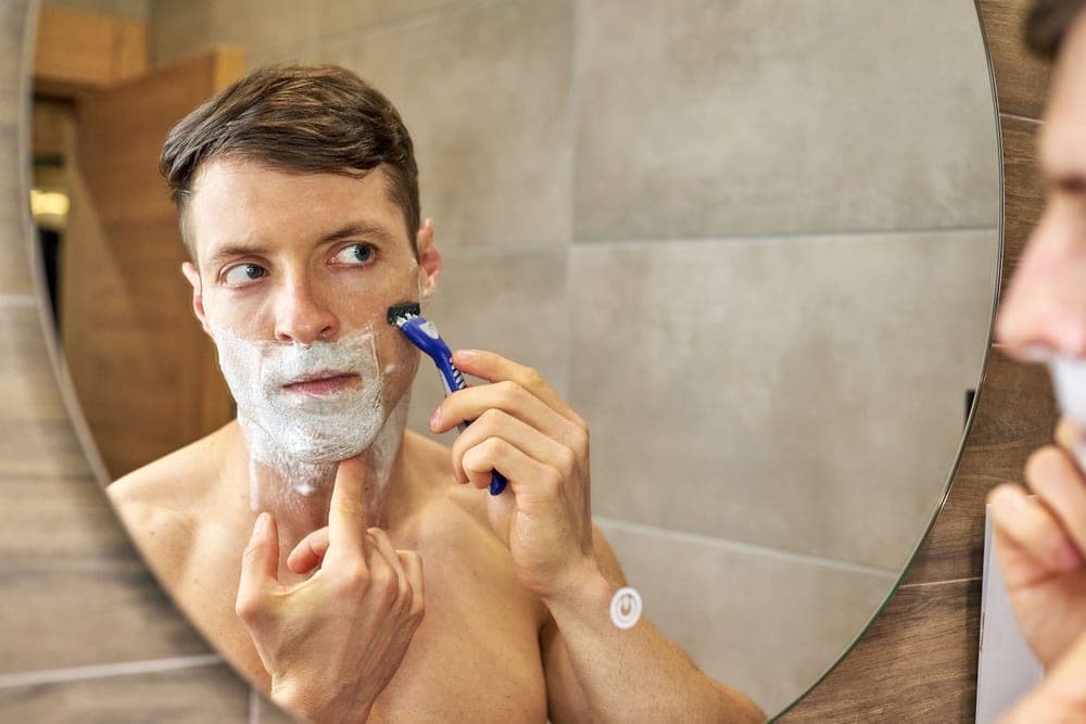 A man shaving his face with a razor in front of a mirror
