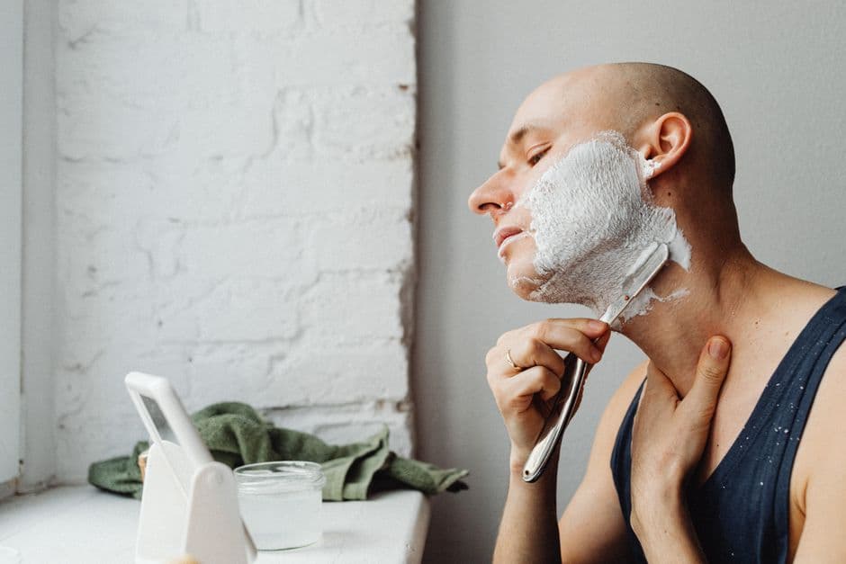 A man shaving his neck at a bathroom mirror