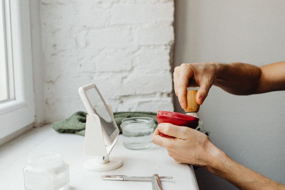 A man's hands working up shaving cream with a brush by a window