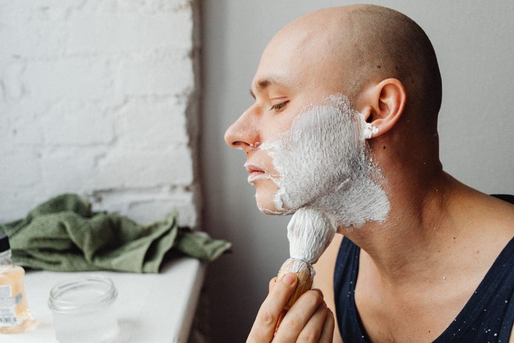 A bowl of shaving soap with lather and a brush beside it