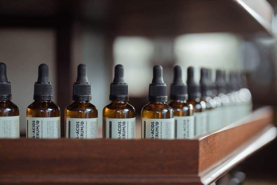 A row of amber serum bottles with dropper caps on a wooden shelf